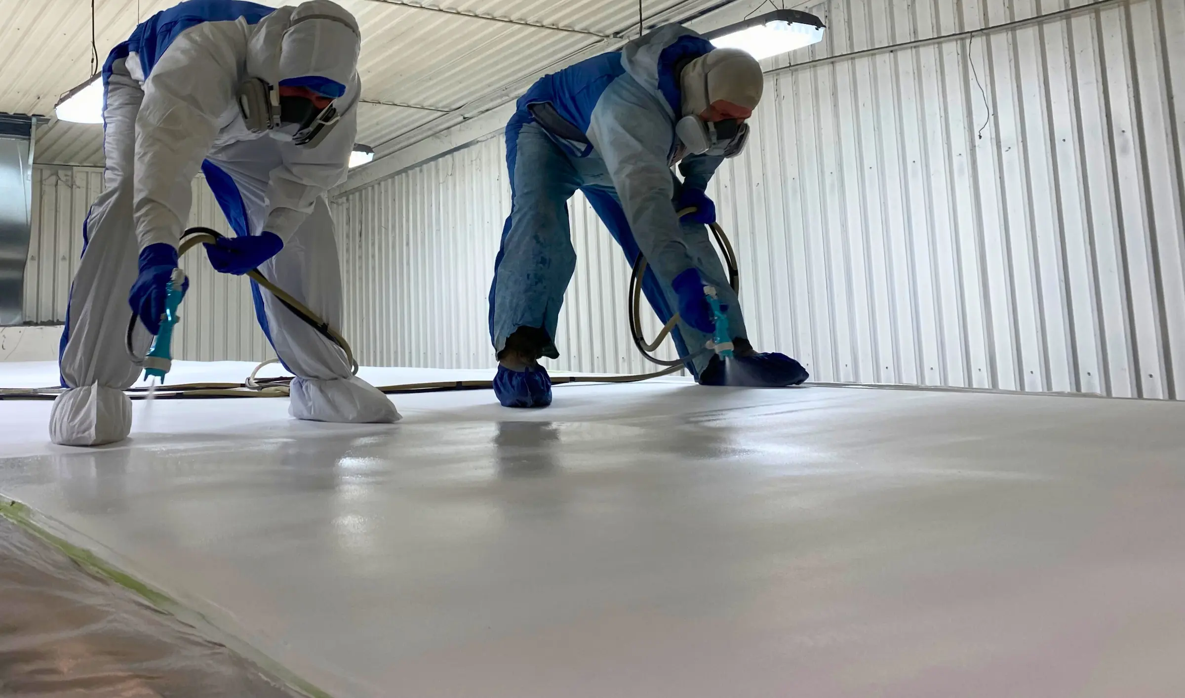 Workers spraying PolyFrost on the top of a trailer in a paint booth.